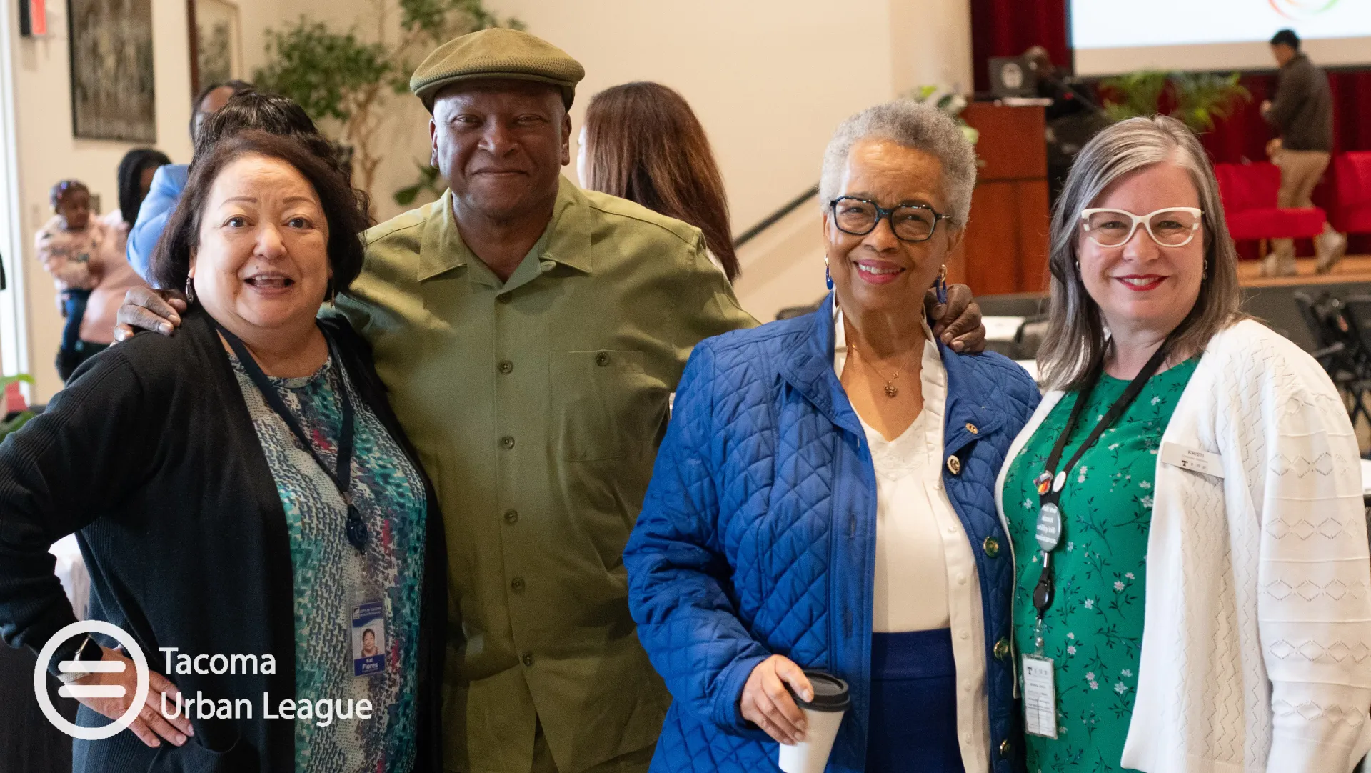 Four Tacoma Urban League community members 40 and older, including three older women and a man in a green shirt and cap, stand together at a gathering