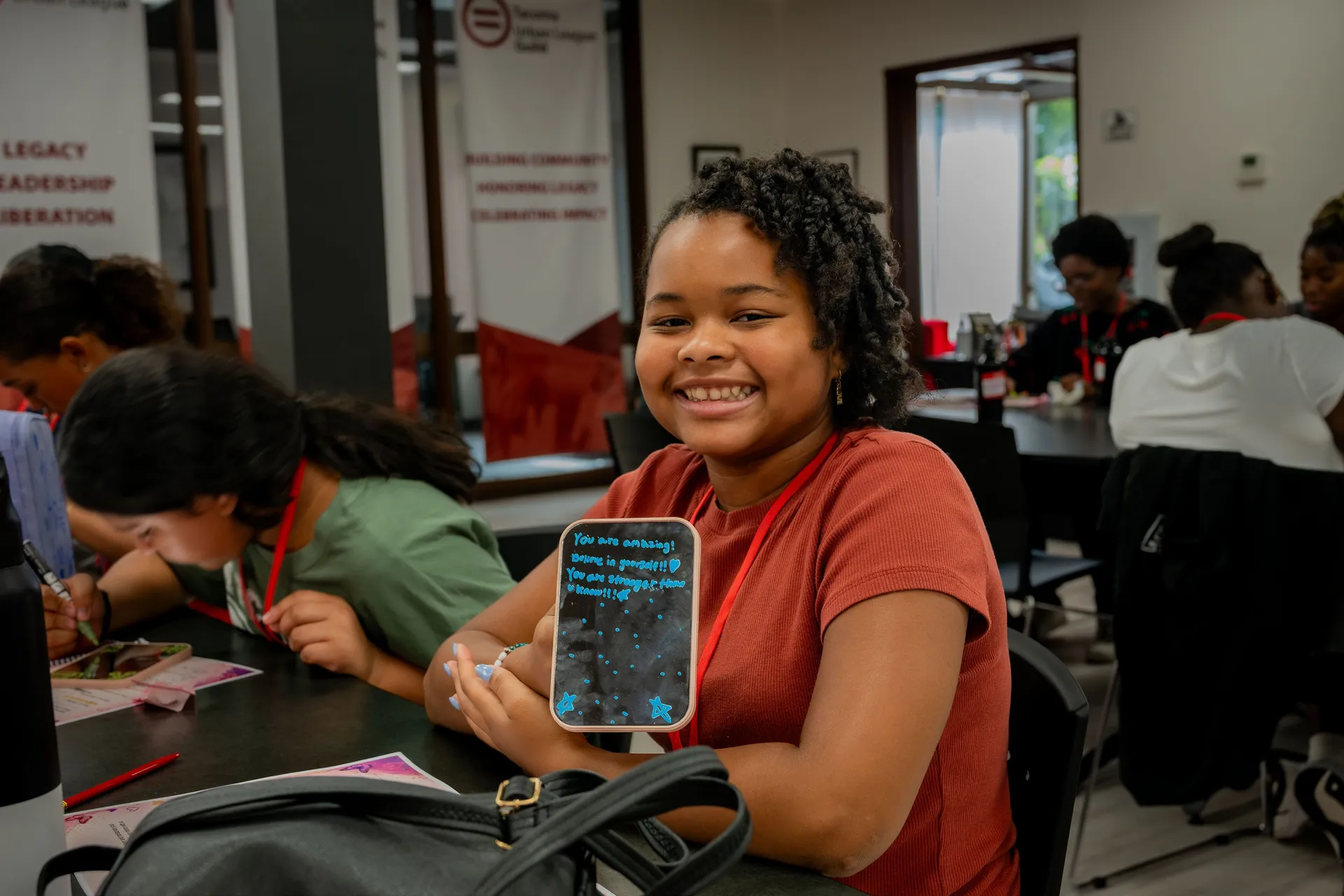 A young student smiles while holding a chalkboard with a written affirmation