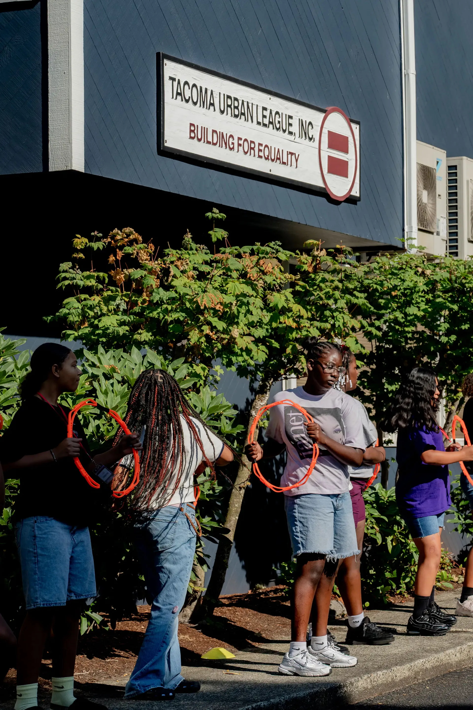 Young people take part in an outdoor activity beneath the Tacoma Urban League Building for Equality sign